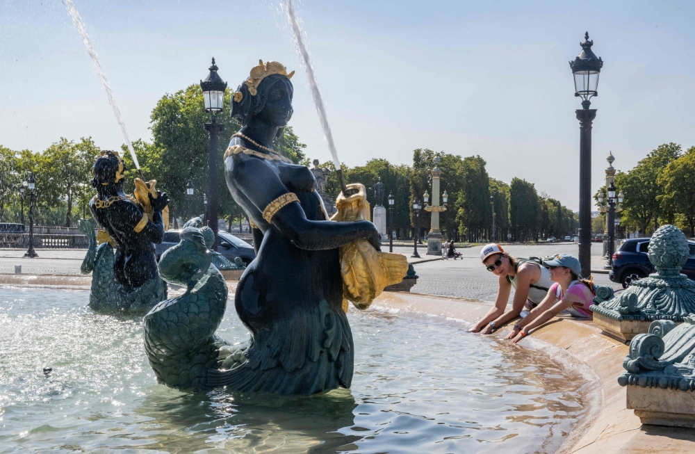 A woman and a child cool their hands in the Fontaine des Mers fountain spraying water at the Place de la Concorde in Paris on August 11, 2025, amid a heatwave in Europe. — AFP pic