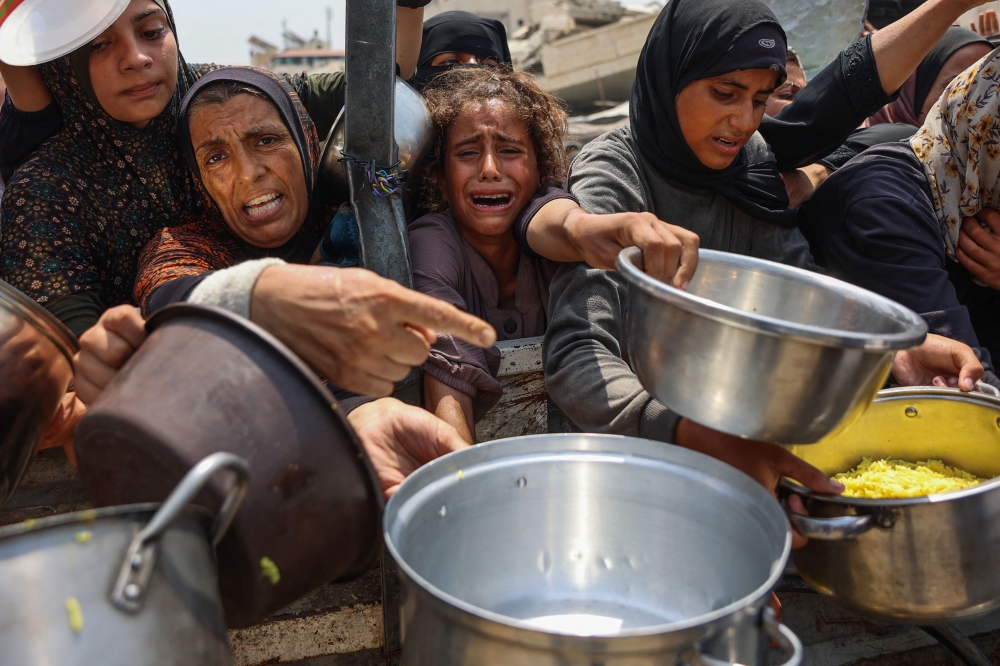 A Palestinian girl cries as she tries to receive cooked meals along with others from a food distribution centre in Gaza City on August 13, 2025. — AFP pic