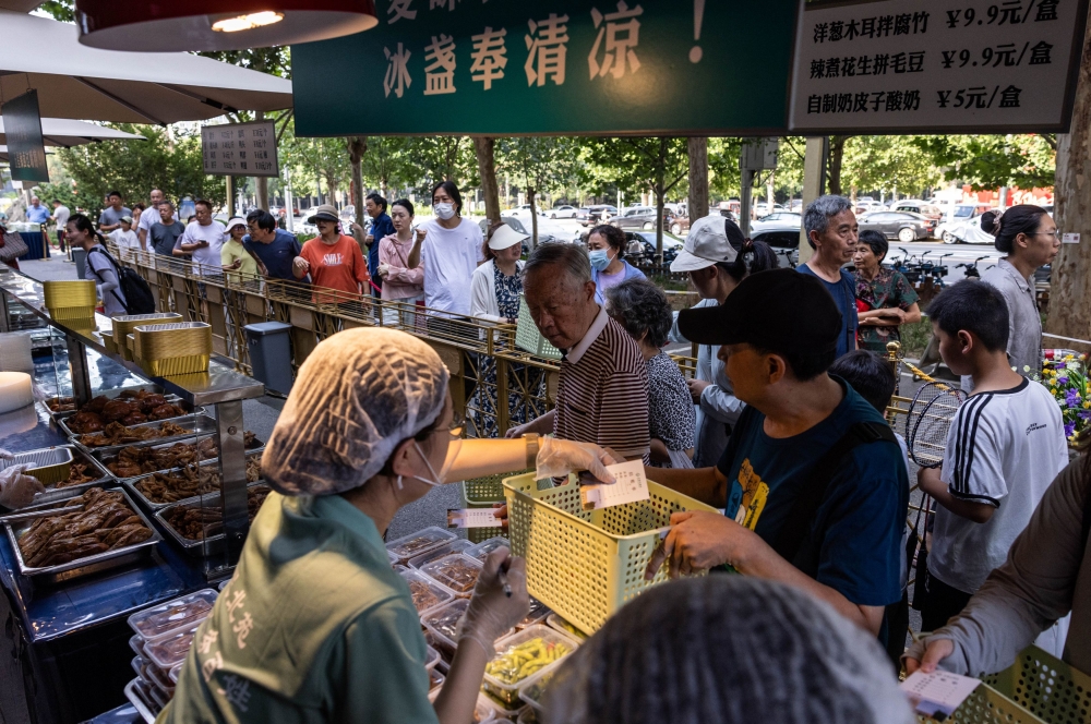 People queue at a setup of stalls selling food, including crispy roast pigeons, to passersby next to Beiyuan Grand Hotel in Beijing August 11, 2025. — Reuters pic