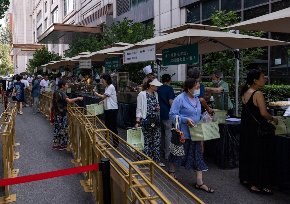 People gather near a setup of stalls selling food to passersby next to Beiyuan Grand Hotel in Beijing August 11, 2025. — Reuters pic  