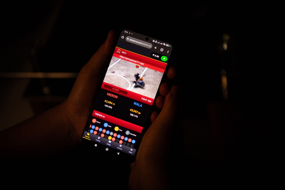 Jay, a graphic artist, watches a live cockfight on his mobile phone in Bulacan province, north of Manila, July 15, 2025. — AFP pic 
