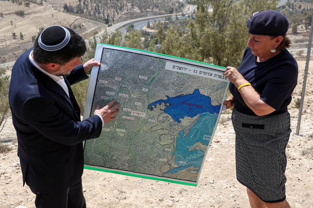 Israeli Finance Minister Bezalel Smotrich and a woman hold a map that shows the long-frozen E1 settlement scheme, that would split East Jerusalem from the occupied West Bank, on the day of a press conference near the Israeli settlement of Maale Adumim, in the Israeli-occupied West Bank, August 14, 2025. — Reuters pic 