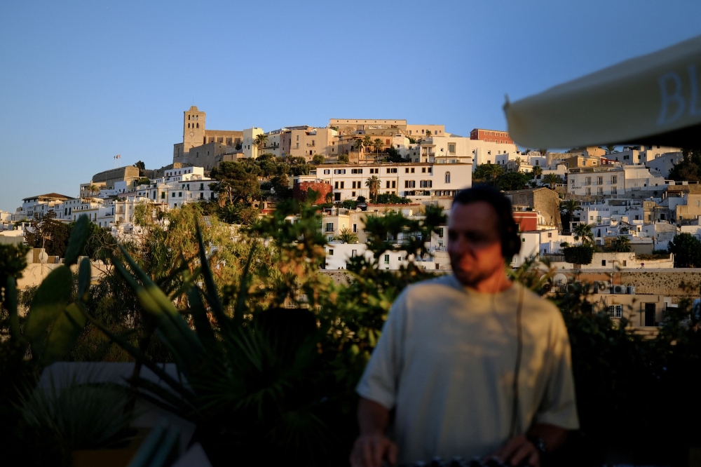 A DJ plays music in front of a castle surrounded by medieval fortifications, at a hotel rooftop in Ibiza, Spain, July 29, 2025. — Reuters pic 