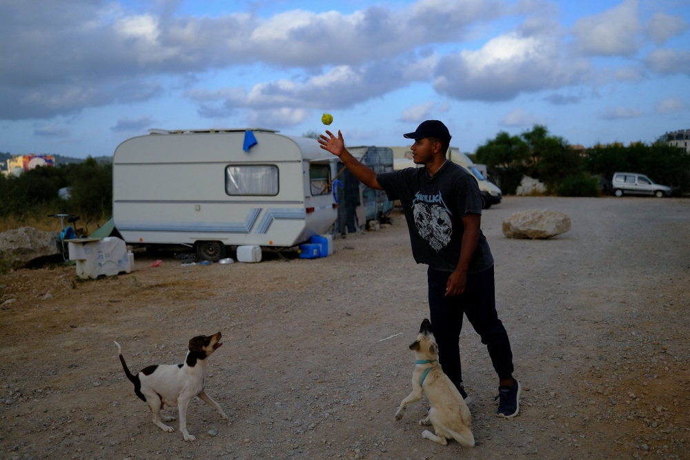 Jonathan Ariza, 25, from Colombia, plays with his dogs in front of the caravan where he lives in Ibiza, Spain, July 28, 2025. — Reuters pic 