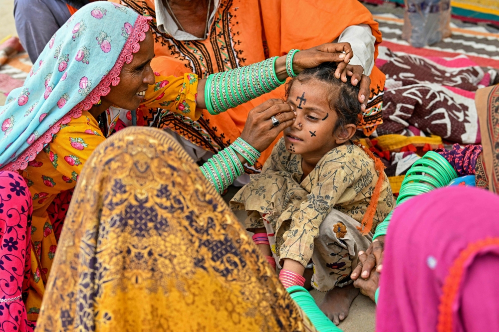 This photograph taken on July 14, 2025 shows artist Guddi Manthar (left), drawing an indigenous tattoo on seven-year-old Champa’s face at the Jogi Colony in Umerkot, a Hindu-majority district in Pakistan. — AFP pic 