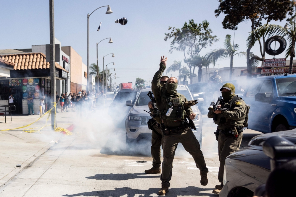 A US Customs and Border Protection officer throws a Stinger CS rubber ball grenade at community members pushing back against a raid attempt on a store in Bell, just south of Los Angeles, California June 20, 2025. Rebuilding is slow, however, because the construction industry relies on skilled migrant workers, the very people being targeted by ICE. — AFP pic