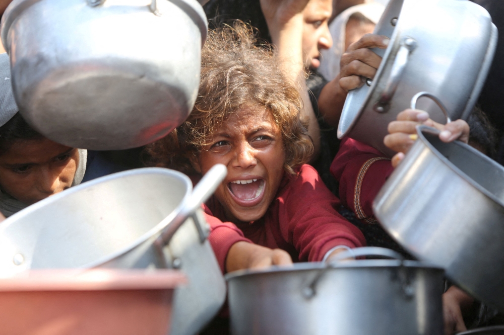 A child reacts surrounded by pots as Palestinians wait to receive food from a charity kitchen in Khan Younis, southern Gaza Strip, August 21, 2025. — Reuters pic