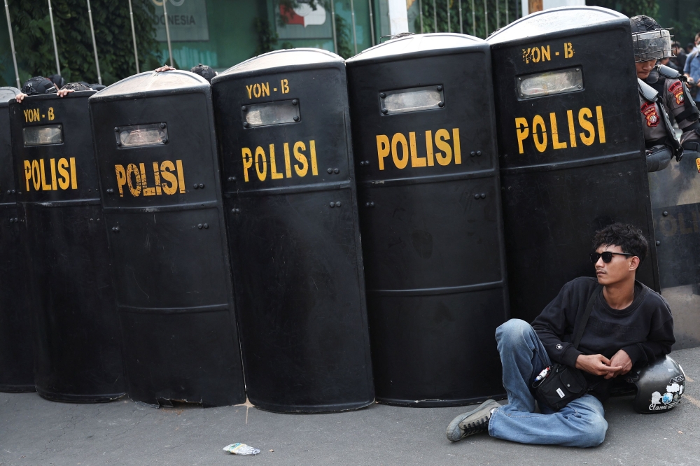 A man sits in front of riot police barricade during a protest against what the demonstrators say are exorbitant allowances for Indonesian parliament members, outside Indonesian parliament buildings in Jakarta, Indonesia, August 25, 2025. — Reuters pic