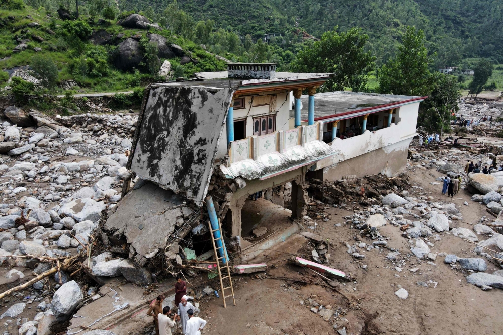 An aerial view shows flood survivors standing near a damaged house surrounded by heavy rocks in the Buner district of mountainous Khyber Pakhtunkhwa province on August 17, 2025. — AFP pic