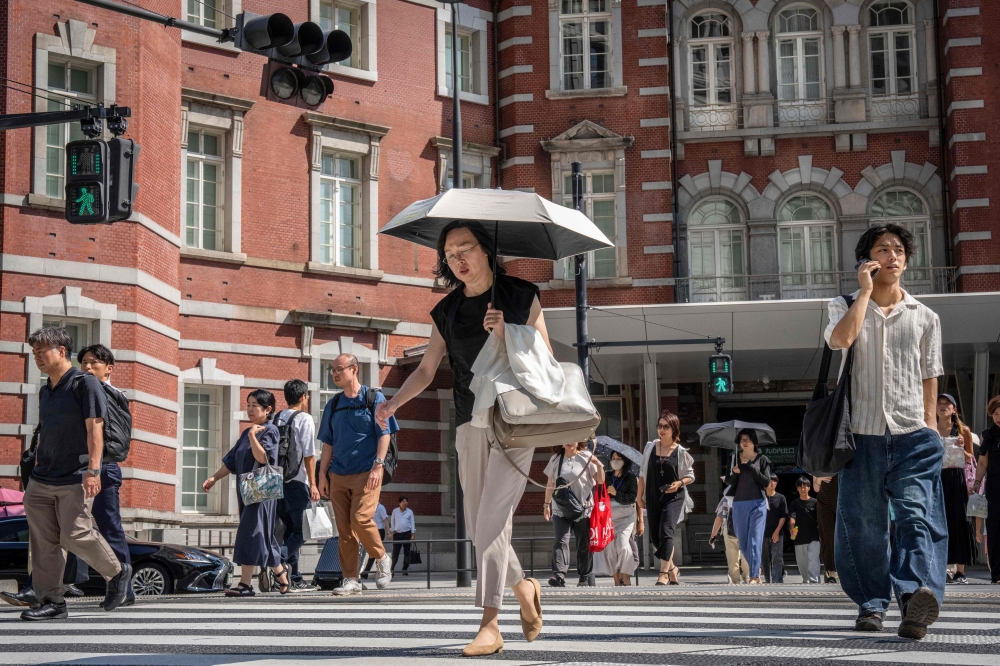 People cross a street outside Tokyo Station on a hot day in Tokyo August 27, 2025. — AFP pic