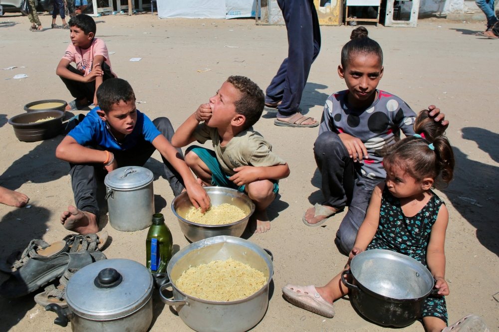 Palestinian children eat cooked rice after managing to get portions of hot food from a charity kitchen in Khan Yunis in the southern Gaza Strip on August 27, 2025. In early March, Israel also sealed off Gaza by land, letting in no supplies for three months, arguing that Hamas was diverting aid. — AFP pic