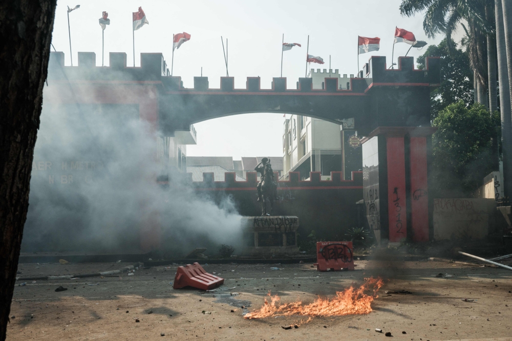 A molotov cocktail burns on the ground amidst a cloud of tear gas in front of the main gate of the headquarters of the Mobile Brigade Corps, or 'Brimob', during clashes with people protesting against the death of a motorcycle taxi driver the night before, in front of the Brimob headquarters in Jakarta on August 29, 2025. — AFP pic