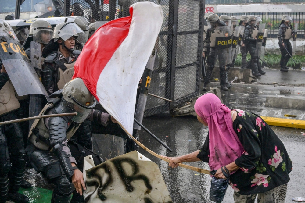 A woman strikes a police officer with a bamboo stick tied to an Indonesian flag as police push back students during a protest outside the parliament building against lawmakers’ demands for higher allowances in Jakarta on August 28, 2025. — AFP pic