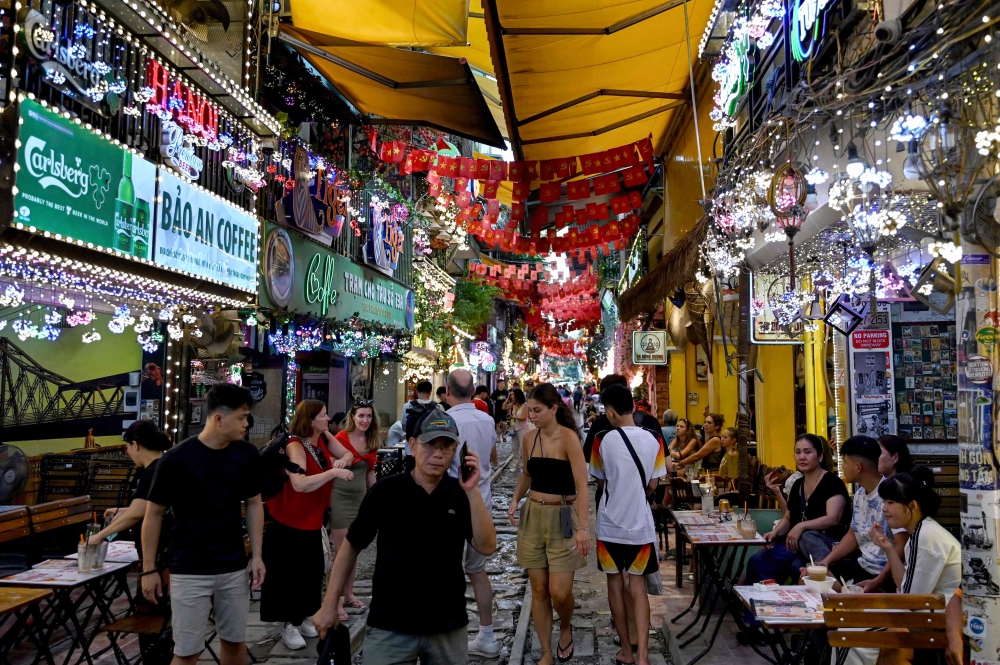 Tourists walks along a railway track between cafe terraces in central Hanoi August 18, 2025. — AFP pic