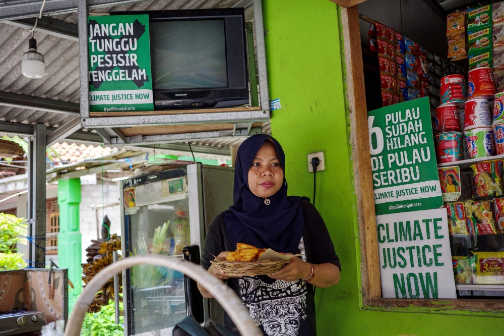 In this picture taken on February 22, 2023, resident Asmaniah serves customers at her food stall adorned with environmental protest messages on Pari island in the Thousand Islands cluster. — AFP pic