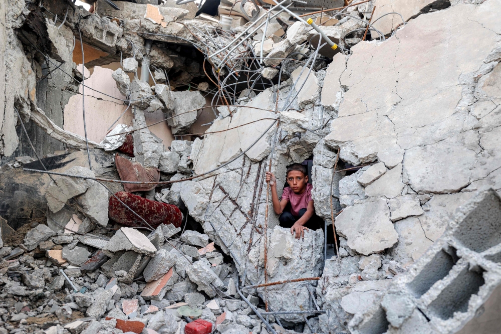 A boy climbs from out of the rubble of a collapsed building that was hit by bombardment in the Nuseirat camp for Palestinian refugees in the central Gaza Strip August 30, 2025. — AFP pic