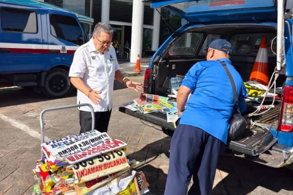Wee (left) helps an MBKS officer unload confiscated illegal banners. — The Borneo Post pic