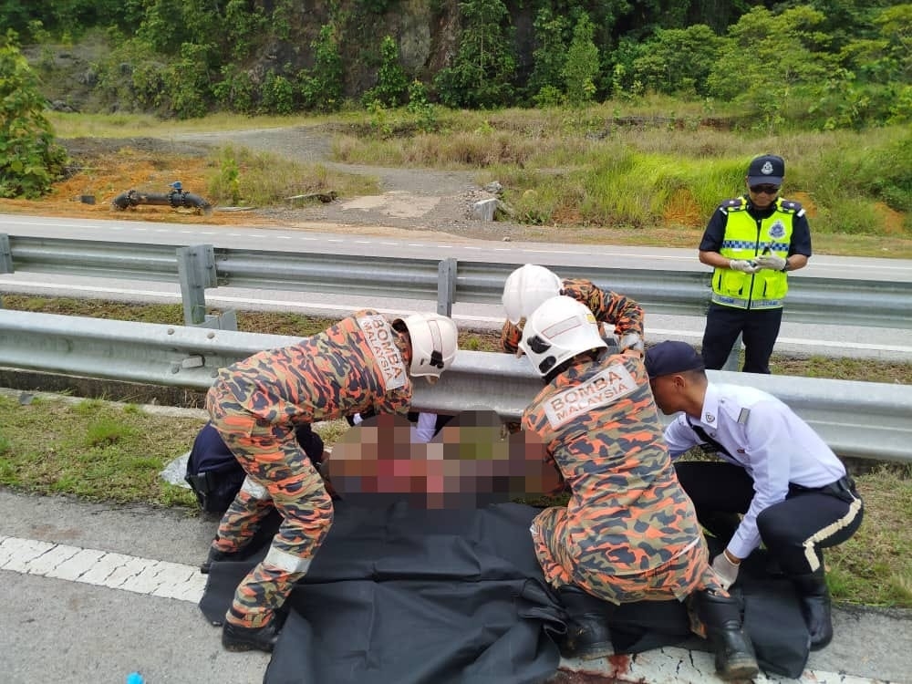 Bomba and police personnel cover up a victim’s body at the scene of the accident. — The Borneo Post pic