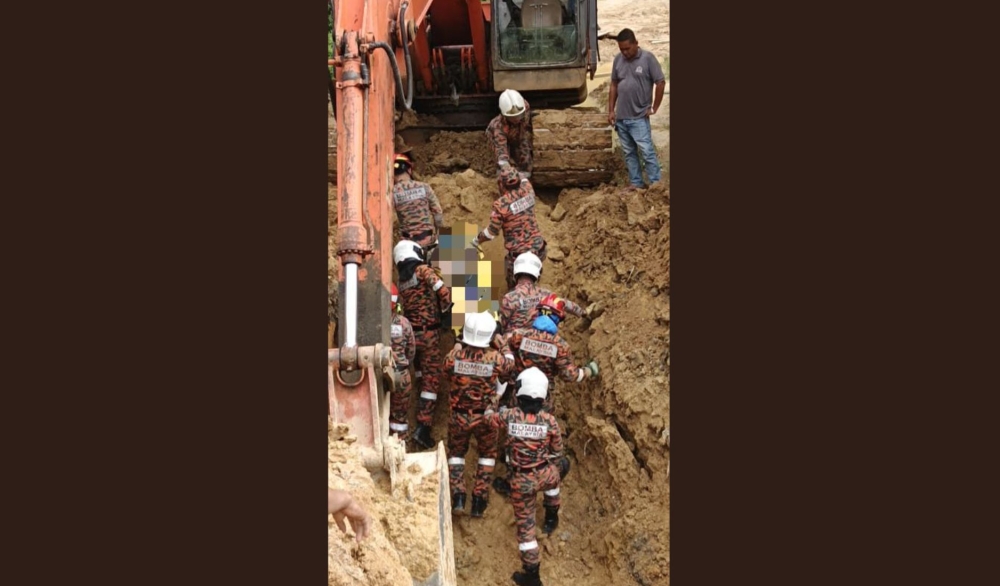Fire and rescue personnel remove the victim’s body from the landslide at the UMS construction site. — The Borneo Post pic