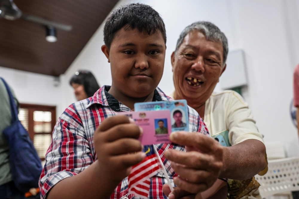 Teoh Zheng Yang (left) holds up his Malaysian MyKad and OKU card at the free Penang Citizenship Programme in George Town on September 7, 2025. — Bernama pic