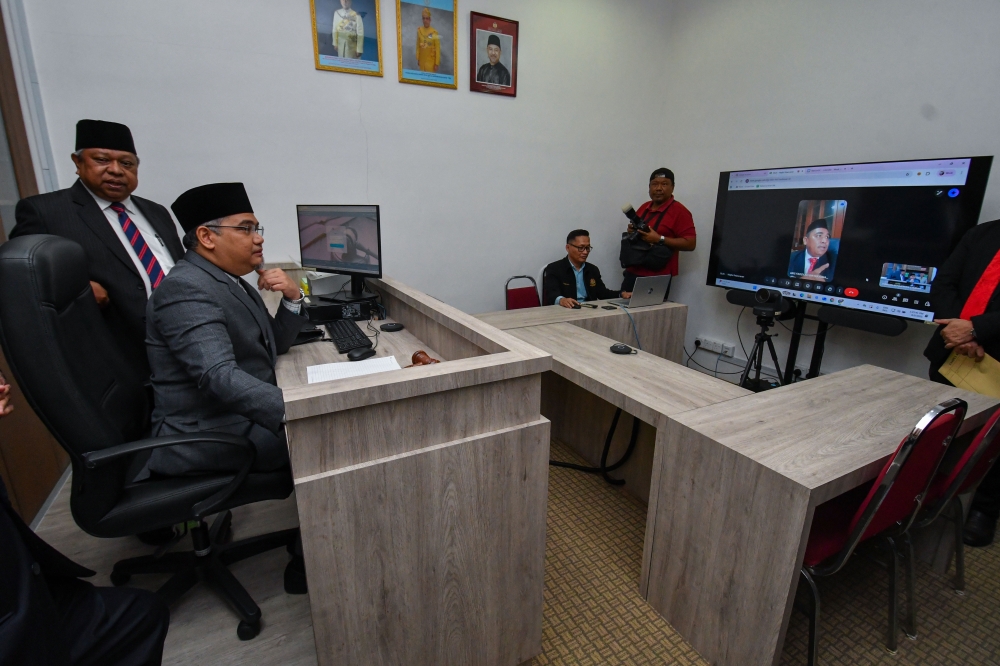 Kelantan Syariah Chief Judge Datuk Ibrahim Deris (left) explains to state executive councillor for Islamic Development, Dakwah, Information and Seranta Relations Mohd Asri Mat Daud (second left) during the launch of the Technology Courtroom at the Kelantan Syariah Court today. Kelantan is the second state after Sarawak to establish the facility for online proceedings. — Bernama pic