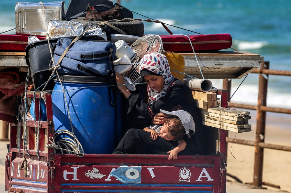 A woman sits with a child as they ride with furniture and belongings in the back of a tricycle cart evacuating them southbound from Gaza City. — AFP pic