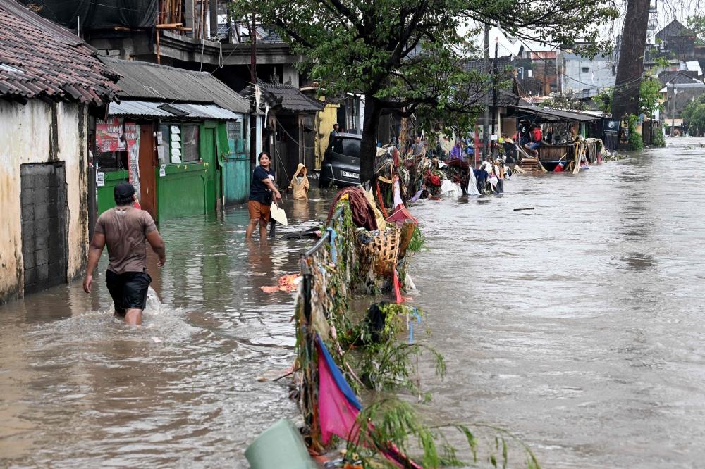 Residents wade through floodwaters in their neighbourhood following heavy rainfall in Denpasar. — AFP pic