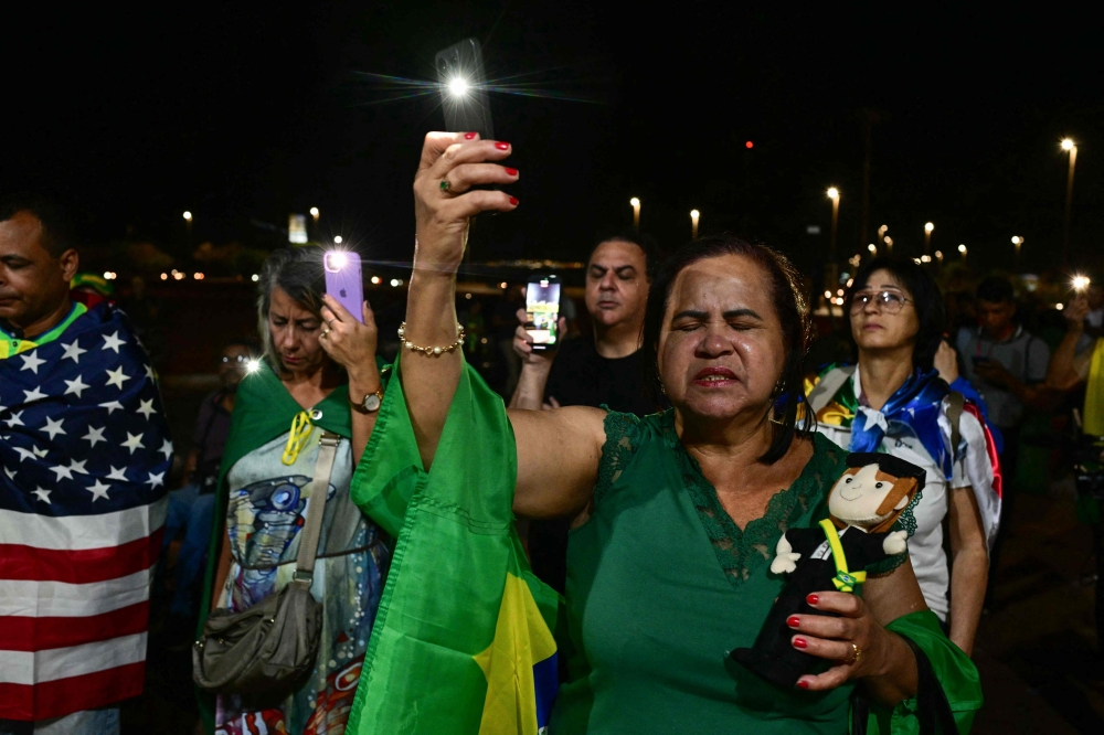 Supporters of former Brazilian President Jair Bolsonaro pray with Brazilian and US flags near his house in Brasilia on September 11, 2025. — AFP pic 