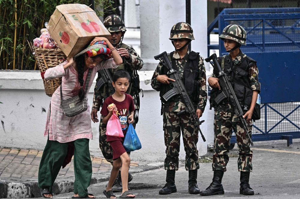 Residents carrying fruits walk past army personnel outside Nepal’s President House during relaxation hours amid a curfew imposed to restore law and order in Kathmandu on September 12, 2025. — AFP pic