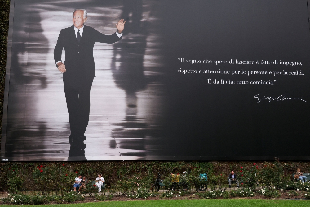 People sit on benches under a billboard with an image of Italian fashion designer Giorgio Armani on the day of his funeral in Milan, Italy, on September 8, 2025. — Reuters pic