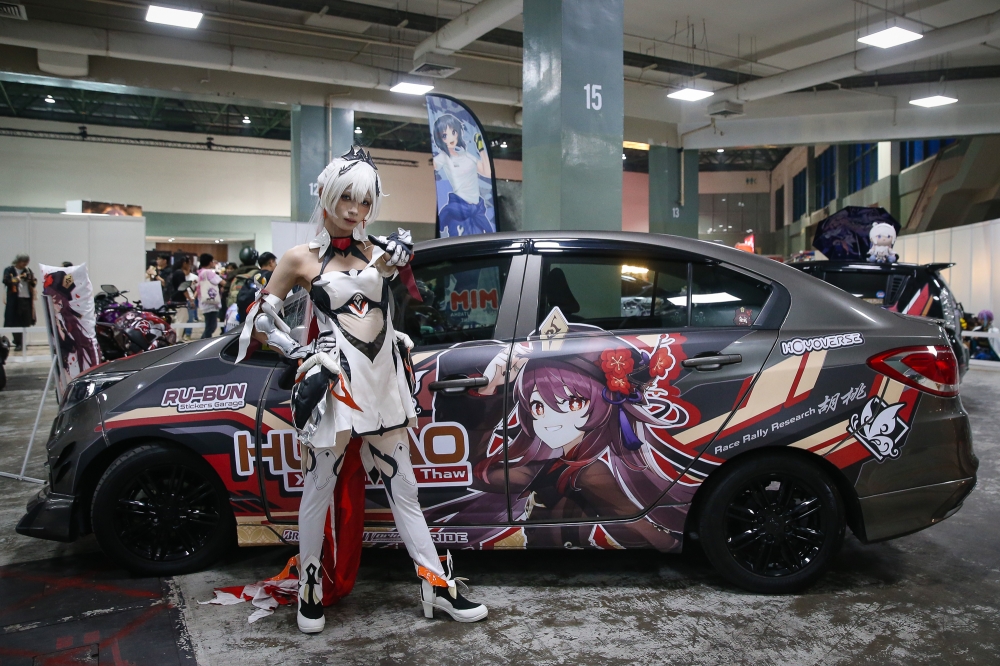A cosplayer posing in front of an itasha decorated with Hu Tao, a character from Genshin Impact during AniManGaki 2025. — Picture by Yusof Isa
