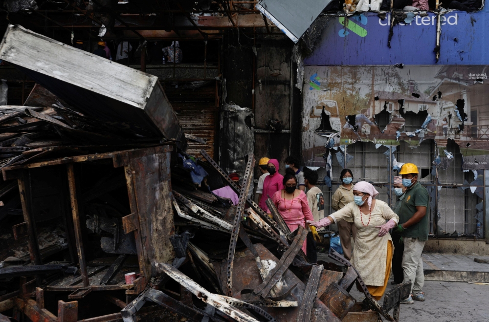 Staff members from Bhat-Bhateni Supermarket works to clears debris from the ransacked building that was torched during the protests. — Reuters pic