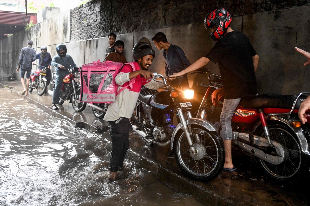Abdullah Abbas, a food delivery rider for Foodpanda, wades through a flooded street under a railway bridge after heavy rainfall in Lahore August 30, 2025. — AFP pic