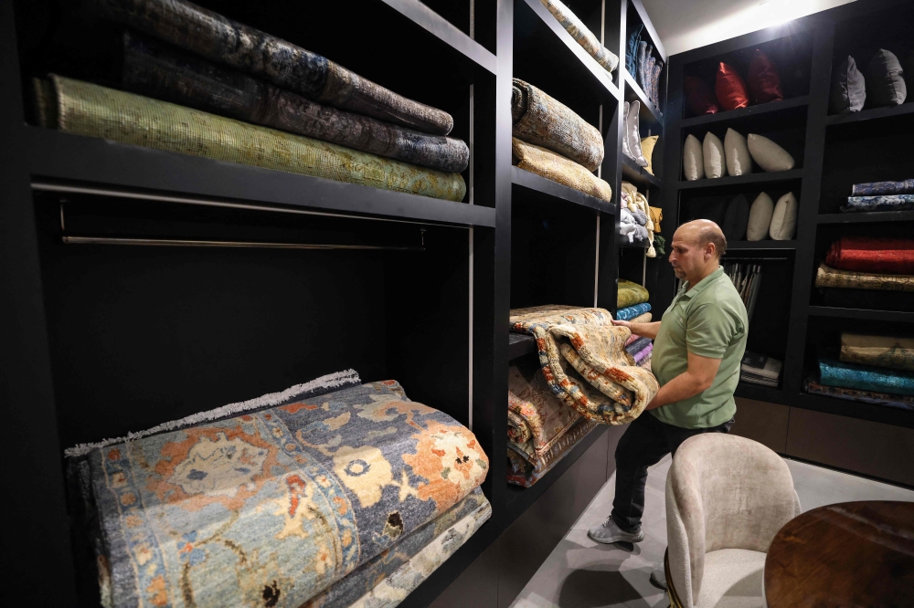 An Iranian seller folds a rug at a shop selling antique and expensive carpets in northern Tehran on September 9, 2025. — AFP pic 