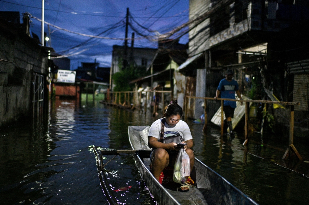 A woman uses her mobile phone while riding a boat through a flooded street after rains intensified by Severe Tropical Storm Bualoi in Dela Paz, Binan, Laguna province, Philippines, September 26, 2025. — Reuters pic
