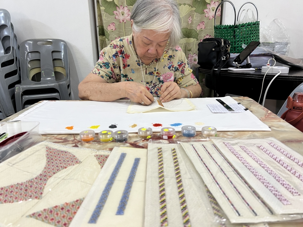 May Lim selects beads and sews them onto the cloth. — Picture by Opalyn Mok