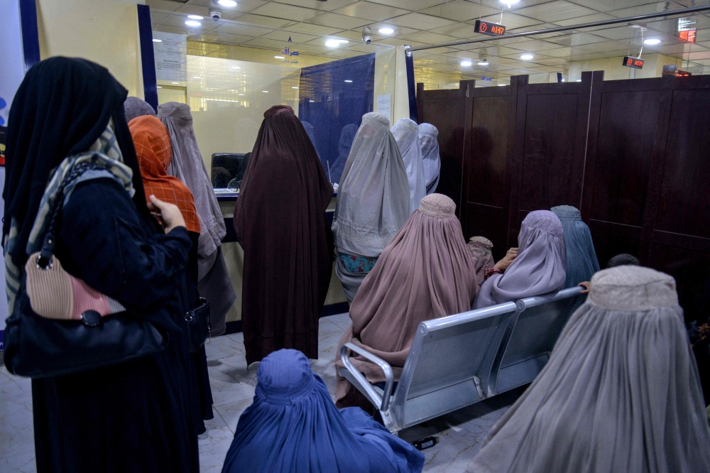 Afghan burqa-clad women wait to withdraw money inside a bank in Kandahar on October 2, 2025. — AFP pic