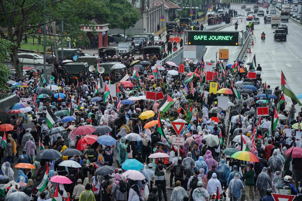 People walk with umbrellas in the rain as they take part in protest near the US embassy here in Kuala Lumpur. — AFP pic