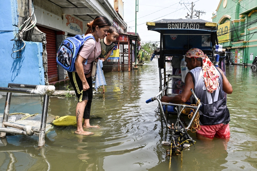 A woman carrying a baby, prepares to ride a pedicab to cross a flooded street, intensified by rain caused by Severe Tropical Storm Matmo, in San Roque, Macabebe, Pampanga, Philippines, October 4, 2025. — AFP pic