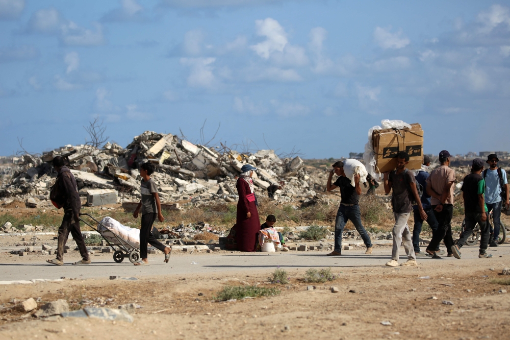 Palestinians carrying bags and empty cardboard boxes walk past a destroyed building as they return from a food distribution point run by the US and Israeli-backed Gaza Humanitarian Foundation (GHF) group, near the Netsarim corridor in the central Gaza Strip on October 5, 2025. — AFP pic