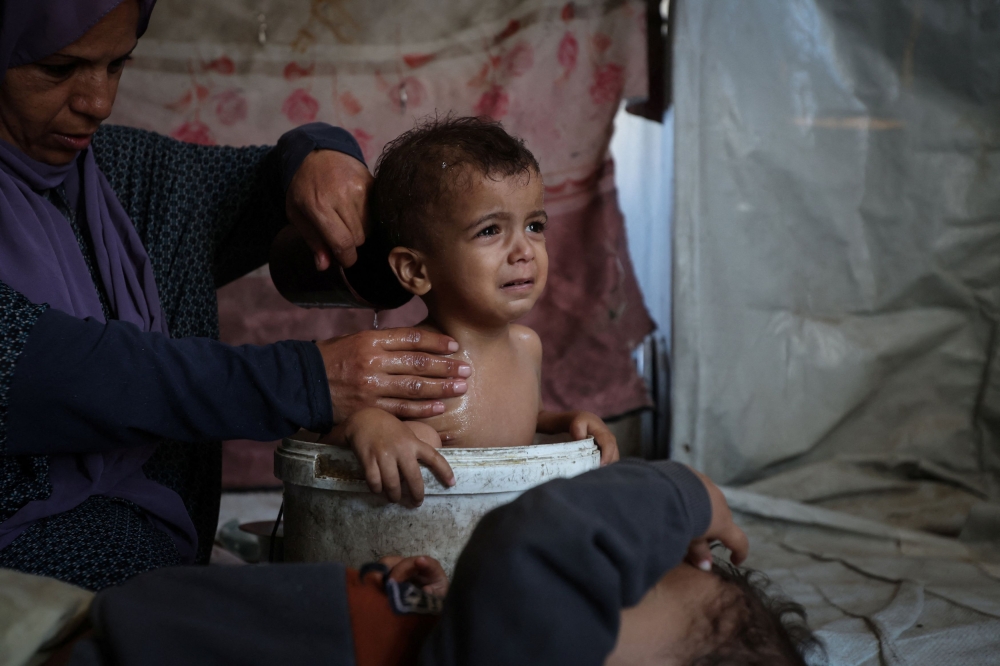 When Iman bathes them, she uses the same bucket that she washes clothes in, the water brought across the camp in heavy plastic containers. — Reuters pic