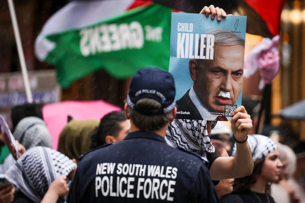 A New South Wales police officer watches pro-Palestinian demonstrators as a placard showing Israeli Prime Minister Benjamin Netanyahu with text that reads ‘child killer’ is seen during a Palestinian solidarity rally in Sydney on October 12, 2025, after two years of conflict in Gaza. — AFP pic