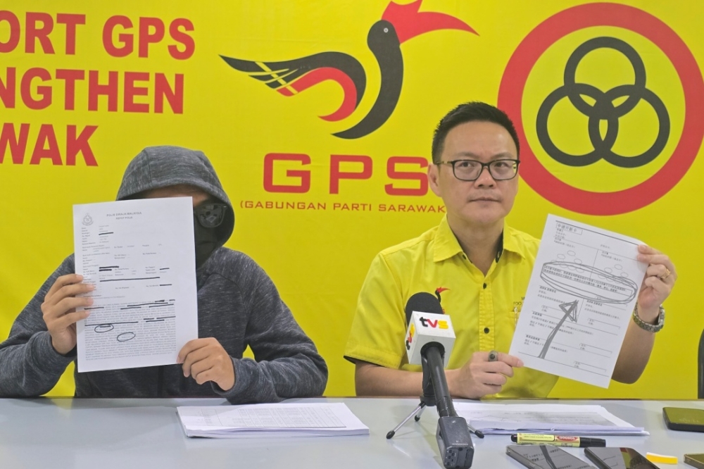 Sarawak United People’s Party Public Complaints Bureau chief Milton Foo shows the form meant for the multi-level marketing scheme, while the victim, on his right, shows the police report. — Galileo Petingi/The Borneo Post pic