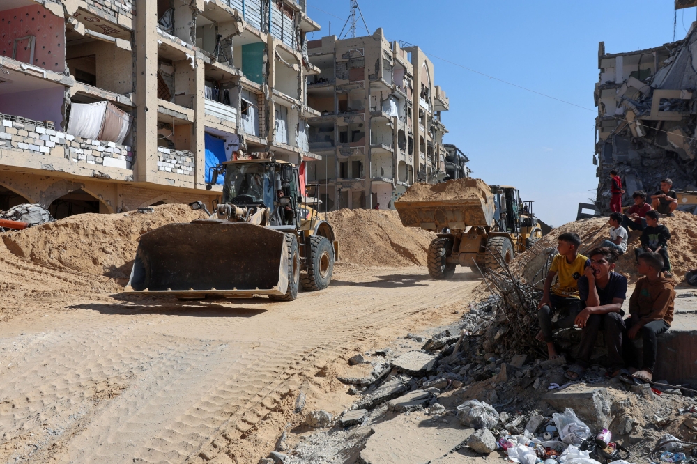 Palestinian children sit near destroyed buildings as heavy machinery operates at a site where searches for deceased hostages kidnapped by Hamas during the October 7, 2023, attack on Israel, are underway amid a ceasefire between Israel and Hamas, in Khan Younis, southern Gaza Strip October 19, 2025. — Reuters pic  
