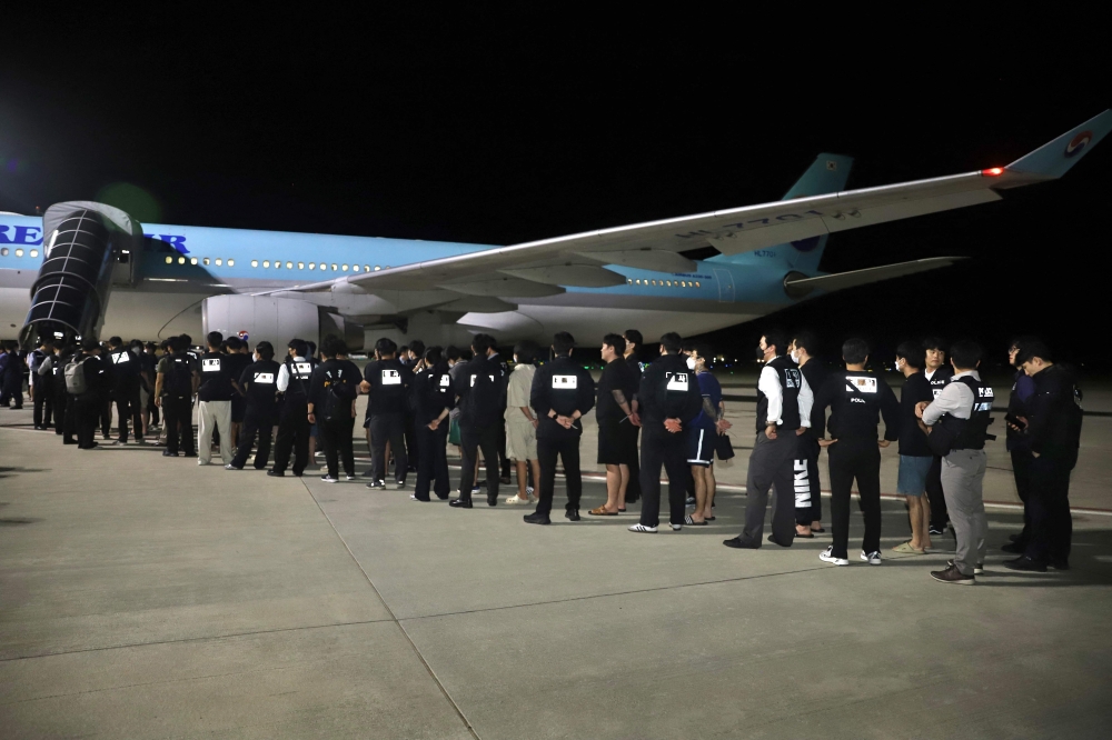 This handout from Agence Kampuchea Press (AKP) taken and released on October 18, 2025 shows South Korean police keeping watch over South Koreans, who had been detained by authorities in Cambodia over alleged cyberscam operations, as they wait to board a chartered plane at Techo International Airport in Kandal province. — Agence Kampuchea Press (AKP) handout/AFP pic 