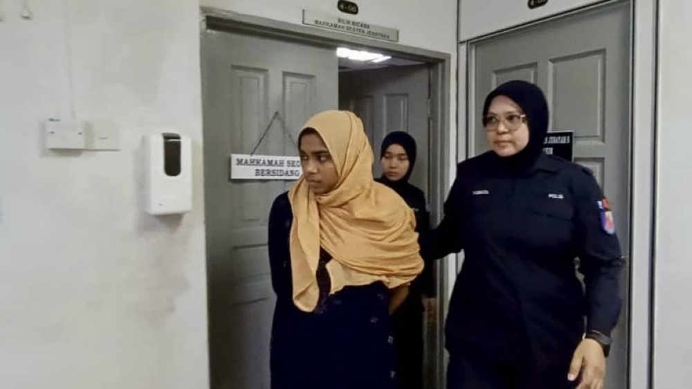 The accused Begum Masuma being escorted by two policewomen at the Johor Bahru court complex October 23, 2025. — Picture by Ben Tan 