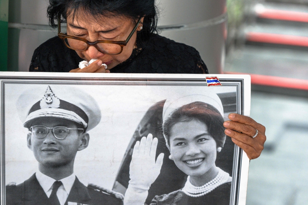 Thai mourner Kanjana Malaithong holds a portrait of Thailand's former queen Sirikit and Thai King Bhumibol Adulyadej as she weeps at Chulalongkorn Hospital in Bangkok on October 25, 2025. — AFP pic