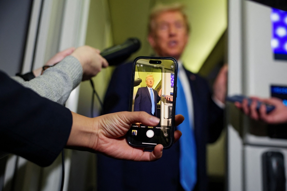 A media member holds their phone in front of US President Donald Trump while Trump speaks to the media aboard Air Force One ahead of his arrival in Malaysia, October 25, 2025. — Reuters pic