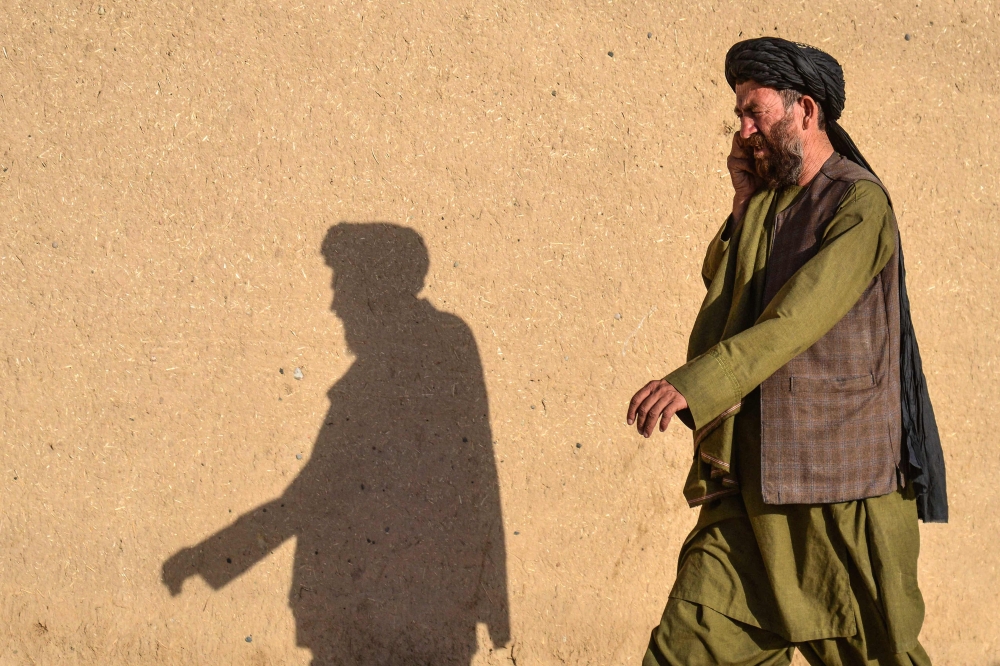 An Afghan man casts a shadow on a wall as he speaks on a mobile phone, along a street in Kandahar on October 26, 2025. — AFP pic