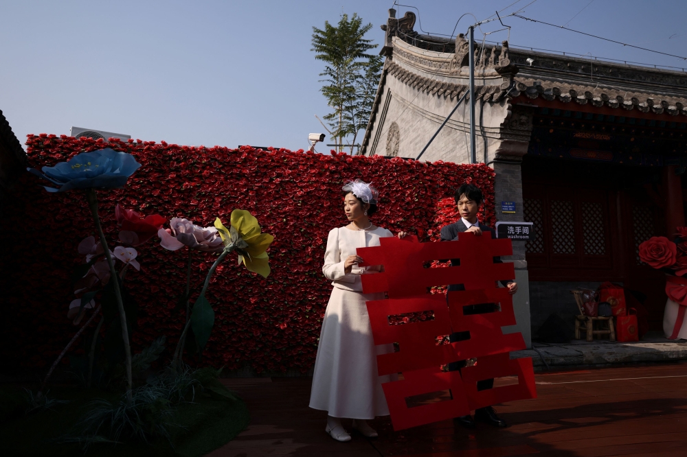 A newlywed couple holding a giant cut-out of the Chinese character Xi, which reads double happiness, pose for pictures after they registered their marriage at the Huguo Guanyin Temple, in Beijing, China, October 28, 2025. — Reuters pic 